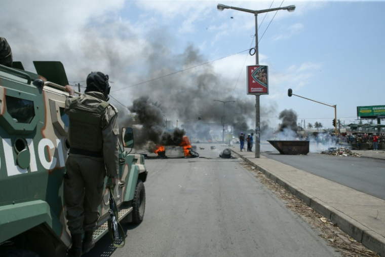 Un agent de police se tenant sur un véhicule blindé face à une barricade de pneus brûlés à Maputo, le 6 décembre 2024 ( AFP / Amilton Neves )