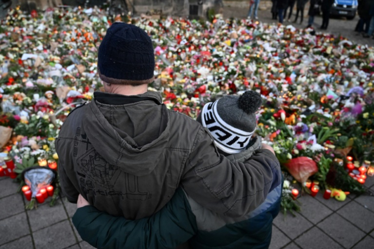 Des personnes se recueillent devant un mémorial de fleurs et de bougies en gommage aux victimes de l'attaque de Magdebourg, le 23 décembre 2024 à Magdebourg en Allemagne ( AFP / RALF HIRSCHBERGER )