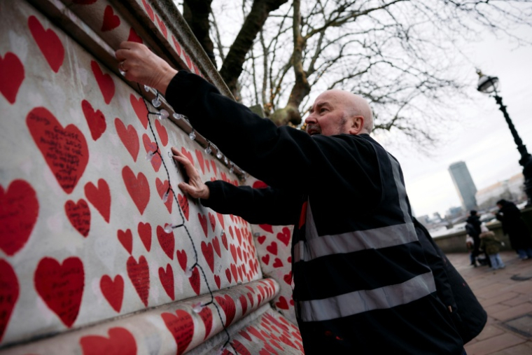 Des bénévoles accrochent une guirlande lumineuse sur un mur dédié aux victimes du Covid, le 20 décembre 2024 à Londes ( AFP / BENJAMIN CREMEL )