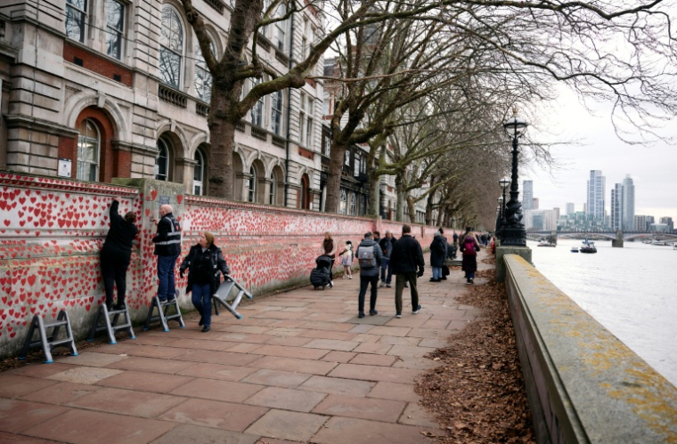 Des bénévoles accrochent des guirlandes lumineuses sur un mur couvert de coeurs rouges en mémoire des victimes du Covid, le 20 décembre 2024 à Londres  ( AFP / BENJAMIN CREMEL )