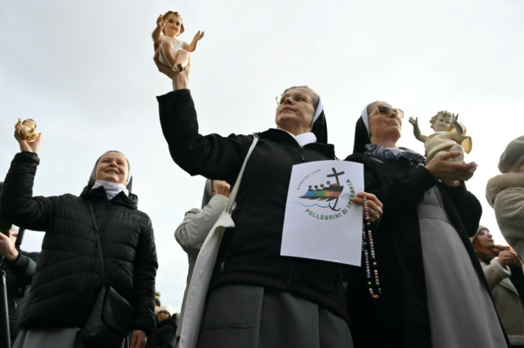 Des religieuses brandissent des figurines de l'enfant Jésus et le logo du Jubilé 2025 lors de la prière de l'Angélus du pape François sur la place Saint-Pierre au Vatican, le 22 décembre 2024 ( AFP / Alberto PIZZOLI )