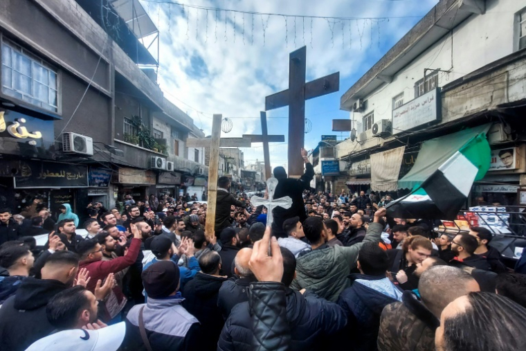 Des Syriens chrétiens brandissent des croix lors d'un rassemblement à Damas, le 24 décembre 2024, pour protester contre l'incendie d'un arbre de Noël près de Hama, dans le centre du pays ( AFP / Louai Beshara )