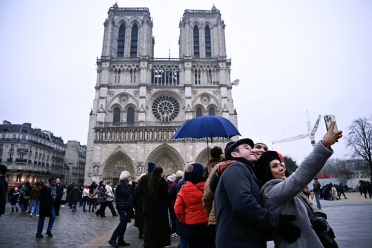 Des personnes prennent un selfie devant Notre-Dame de Paris, le 24 décembre 2024 ( AFP / JULIEN DE ROSA )