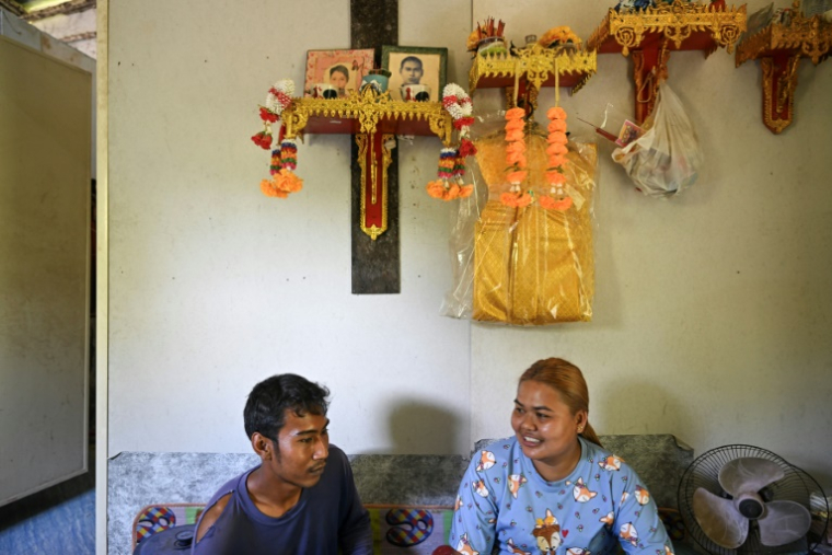 Pirun Kla-Talay et son épouse Janjira Khampradit assis dans leur maison sous les portraits des parents de Pirun, morts dans le tsunami de 2004, le 19 novembre 2024 dans la province de Phang Nga, le 19 novembre 2024 en Thaïlande ( AFP / Manan VATSYAYANA )