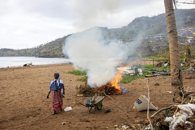 Une habitante de Mayotte fait brûler des branches de palmiers arrachées sur la plage à Acoua, le 25 décembre 2024 ( AFP / PATRICK MEINHARDT )